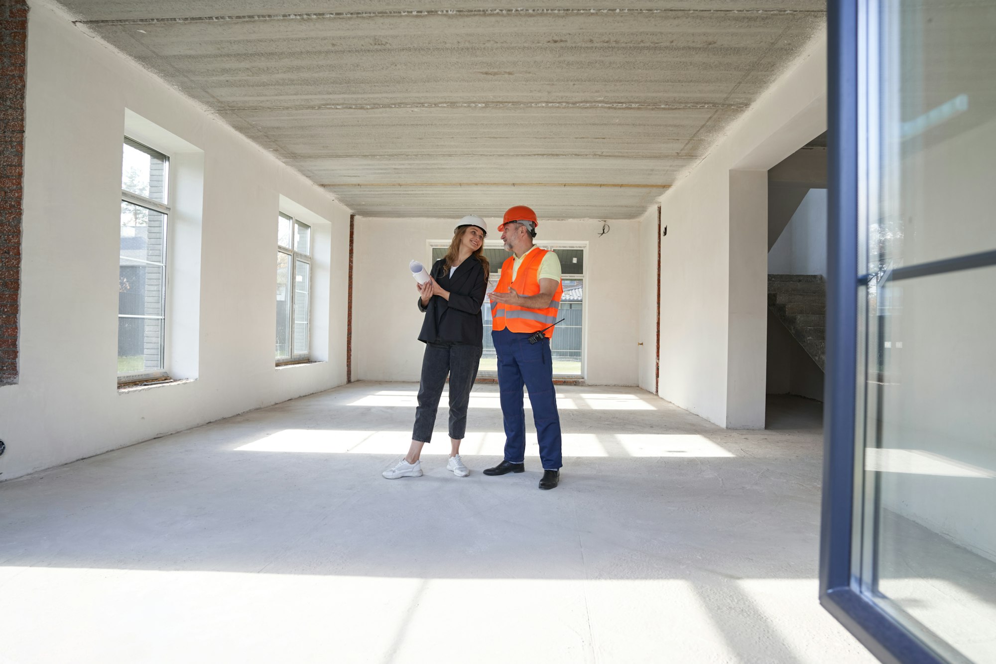 Woman engineer talking with construction worker inside house